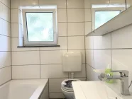 Badezimmer mit Fenster, Wanne, Waschbecken und WC