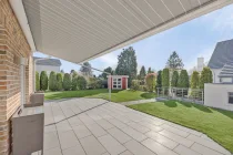 Blick über die ca. 75m² große Terrasse zum Gartenhaus und Zugang Abstellraum/ Garage